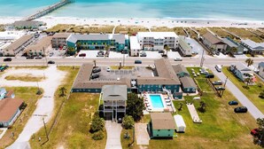 An aerial view of a coastal hotel with multiple buildings, a swimming pool, and a pier extending into the ocean. - Seabirds Motel At Kure Beach (Kure Beach)