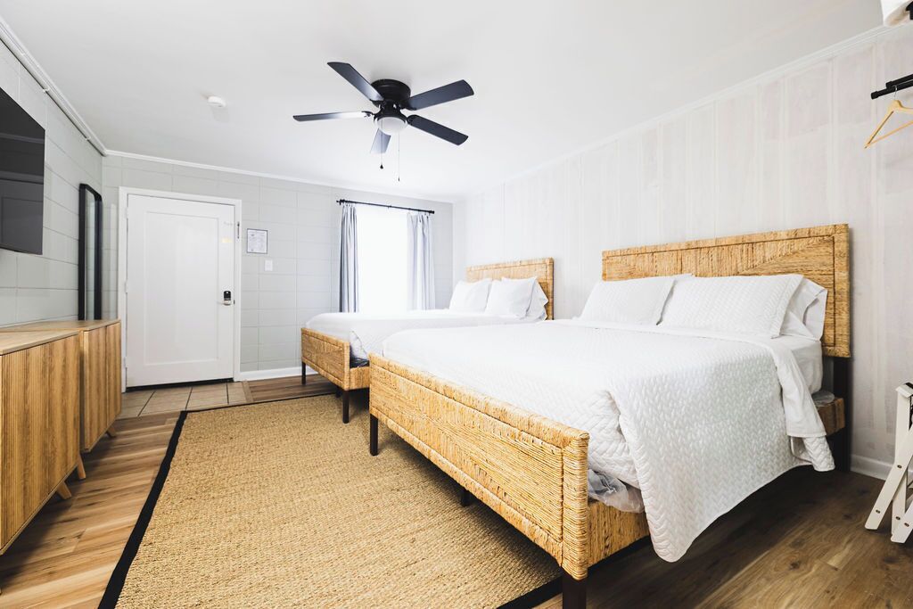 A modern bedroom with a large bed, a ceiling fan, a wooden headboard, and a small bedside table.