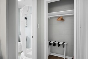 A walk-in closet with a white door, a hanging rack, and a white shelf with black hangers.