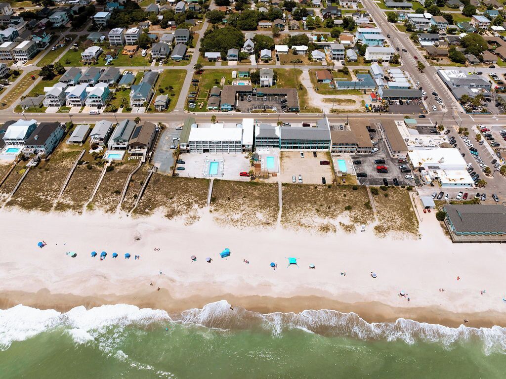 An aerial view of a coastal residential area with houses, a beach, and a large building with a swimming pool.
