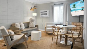 A modern living room with a sofa, chairs, a coffee table, and a TV displaying a beach scene. - Seabirds Motel At Kure Beach (Kure Beach)