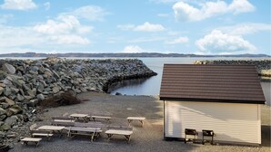 A beachside area with a rocky breakwater, a small shed, and several wooden benches. - 4 bedroom cozy home in Sveio (Sveio)