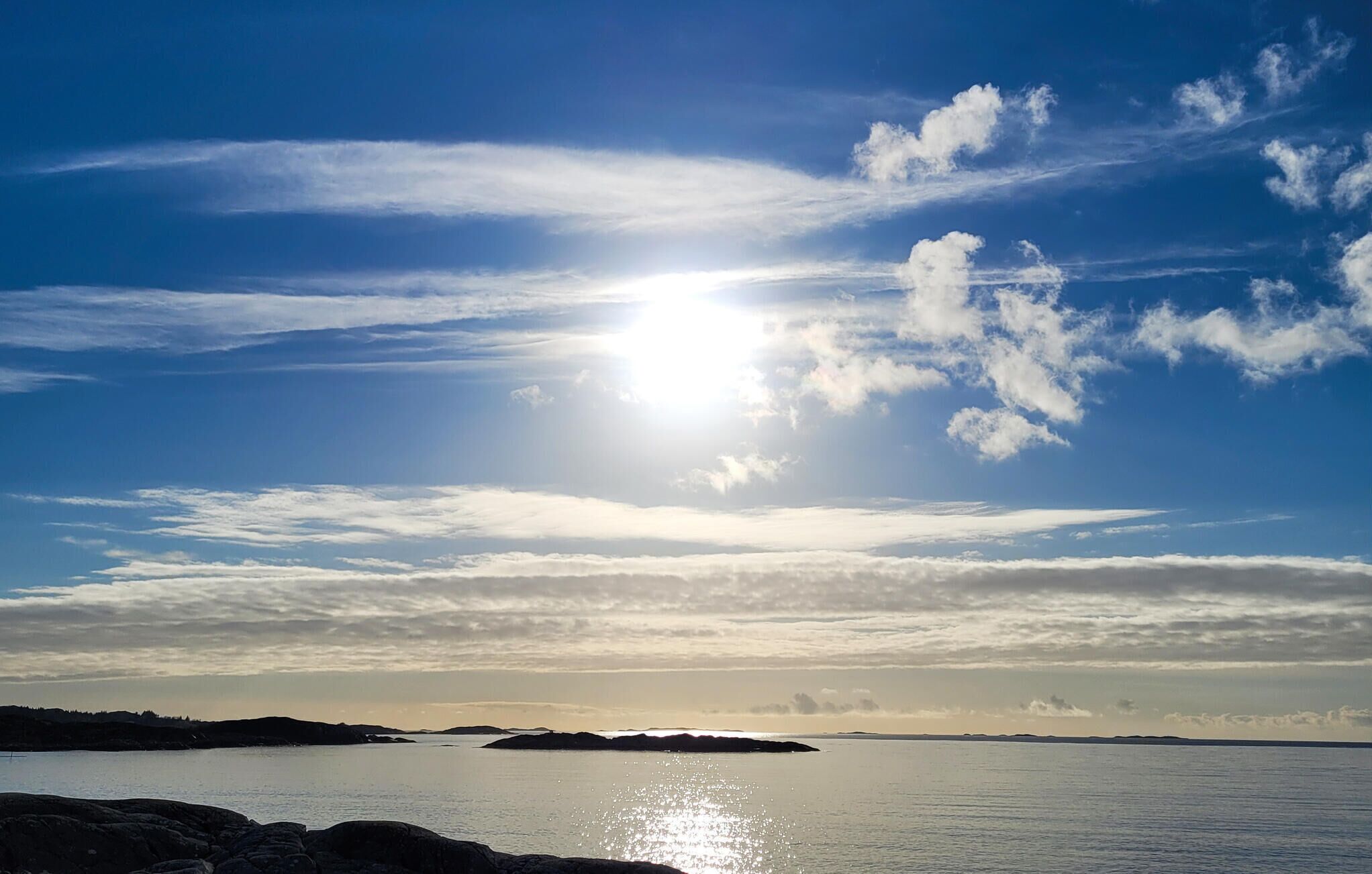Un ciel dégagé, le soleil brillant à travers les nuages, une étendue d’eau calme et des reliefs lointains.