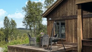 Een houten chalet met een terras, twee rieten stoelen, een schommel en een raam met het nummer 22.