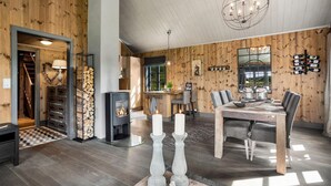 Een modern interieur met een houten wand, een eetgedeelte met een tafel en stoelen, een open haard en een kroonluchter.