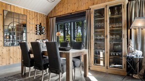 Een kamer met houten lambrisering, een eettafel met stoelen, een wijnrek en een kast met glazen deuren.