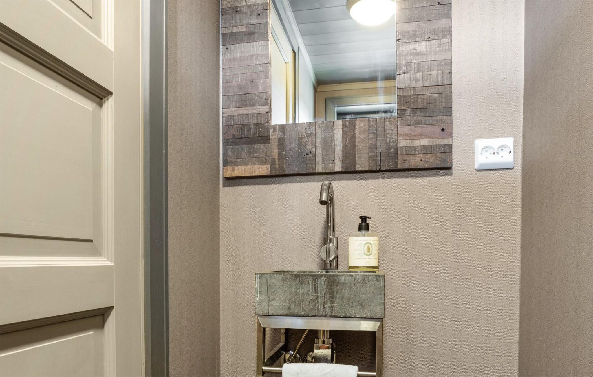 A bathroom with a wooden-framed mirror, a sink with a soap dispenser, and a towel hanging on a rack.