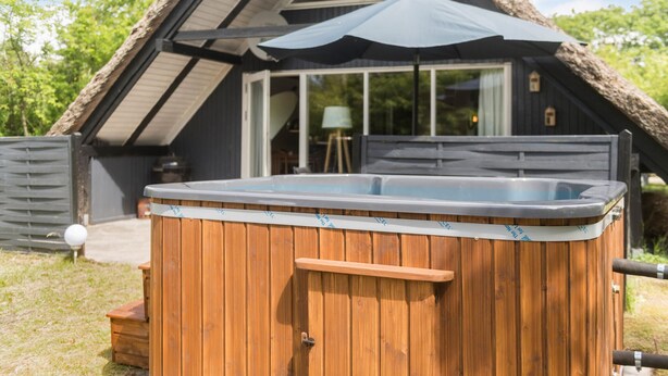 A wooden hot tub with a built-in bench, positioned in front of a house with a sloped roof and a large window. - Beautiful home in Hemmet with WiFi (Hemmet)