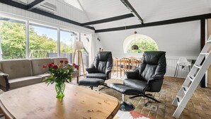 A spacious room with a high ceiling, large windows, a wooden coffee table, a sofa, two leather chairs, and a dining area with a table and chairs. - Beautiful home in Hemmet with WiFi (Hemmet)