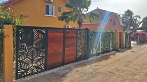 A residential house with a yellow facade, a gated entrance with a decorative metal gate, and a dirt driveway. - 2 Bedroom Villa in Saly (Saly)
