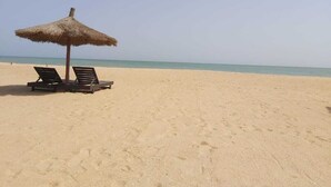 A beach with two lounge chairs under a thatched umbrella. - 2 Bedroom Villa in Saly (Saly)