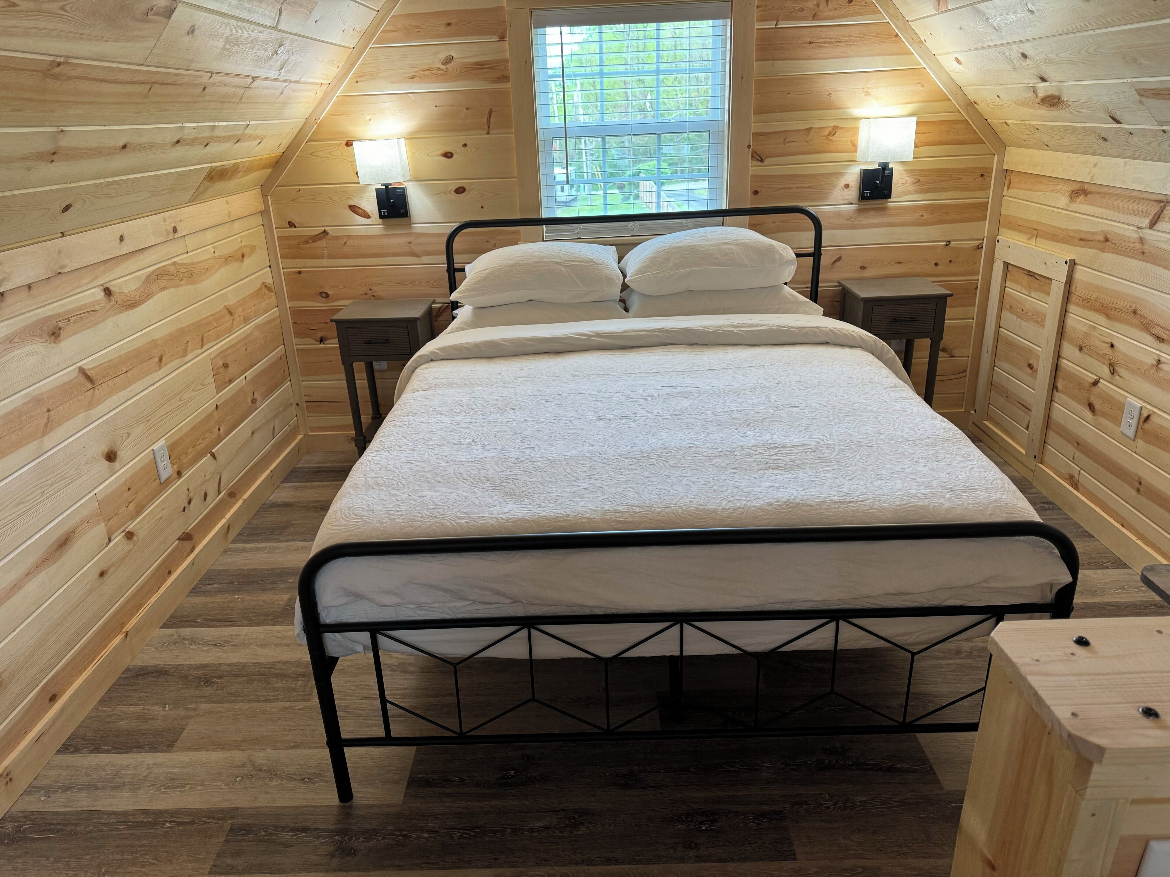 A wooden cabin bedroom with a bed, two bedside tables, and a window.