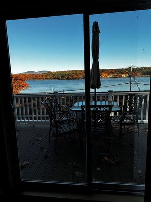 A deck with a table and chairs, overlooking a body of water and autumn foliage.