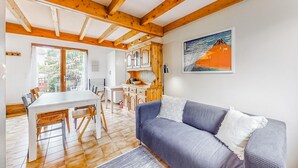 En hyggelig stue med træloft, et spiseområde med bord og stole, og et køkken med træskabe.
