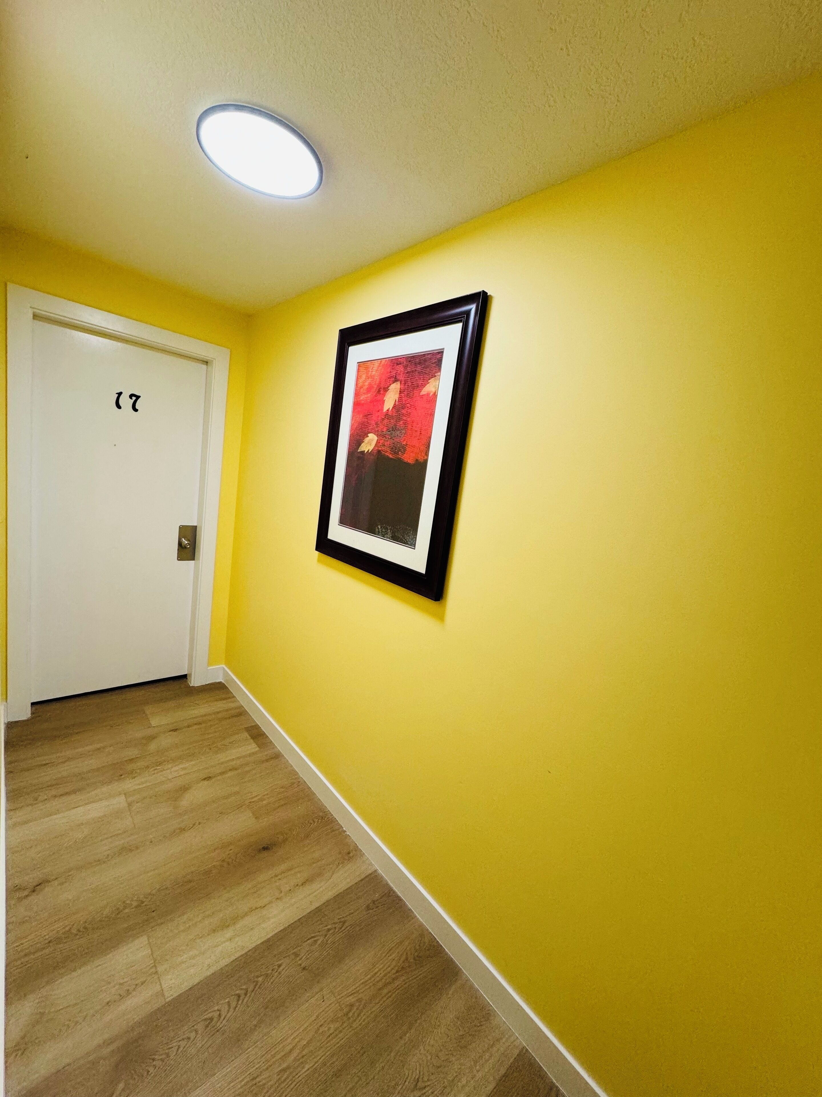 A hallway with yellow walls, a framed picture, and a white door with a number.