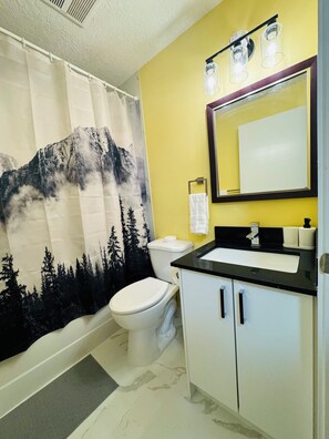 A bathroom with a mountain-themed shower curtain, a white toilet, a black sink with a mirror above it, and a white cabinet. - Avola Mountain Lodge (Avola)