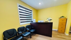 Zona de recepción con escritorio de madera, una computadora portátil y un jarrón de flores. Hay tres sillones de cuero negro y un mueble de madera.