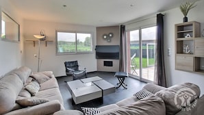 Un salon moderne comprenant un ensemble de canapés, une table basse, un fauteuil et un téléviseur fixé au mur.