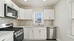 Una cocina moderna con armarios blancos, un microondas de acero inoxidable, una estufa a gas y un lavavajillas.