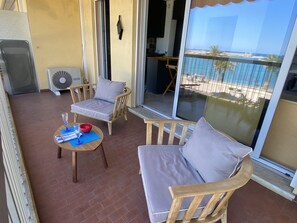 Un balcon avec deux chaises en bois et une petite table, un ventilateur et une vue sur la plage.