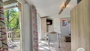 Un interior moderno con suelo de madera, una zona de comedor con mesa y sillas, un televisor montado en la pared y vistas al exterior a través de un ventanal.