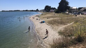 Una playa con agua cristalina, gente caminando y nadando, y algunos paraguas en la arena.