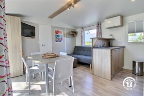 Een ruimtelijke leefruimte met een eettafel, stoelen, een bank, een kitchenette en een aan de muur bevestigde televisie.