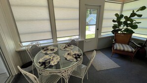 Un invernadero con una mesa de vidrio rodeada de sillas, una silla de mimbre y una planta en maceta.