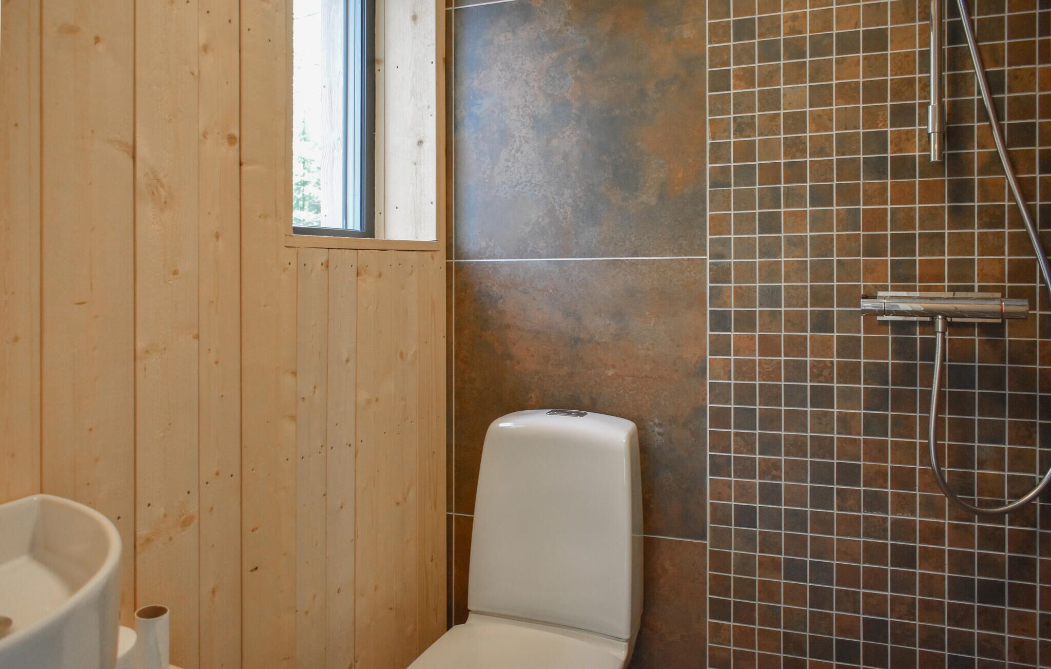 Ein Badezimmer mit Holzwänden, einer weißen Toilette und einem gefliesten Duschbereich.