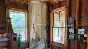 Ein gemütliches Zimmer mit einer Holztreppe, einer Hängematte, einem Fenster mit Blick auf Grünflächen und einem Regal mit Büchern und einem Schild mit einem Hummer darauf.