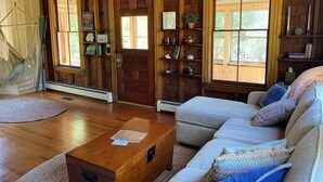 Ein gemütliches Blockhauss-Interieur mit Holzboden, einer Couch, einem Couchtisch aus Holz und einer Hängematte.