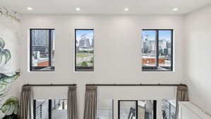 A room with three windows, a ceiling with recessed lighting, and a view of a cityscape. - Beverly Nash, Incredible Skyline Views! Pool & Gym, Walk to Broadway (Nashville)