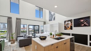 A modern kitchen with a central island, a dining area with a grey sofa, and a view of the cityscape through large windows. - Beverly Nash, Incredible Skyline Views! Pool & Gym, Walk to Broadway (Nashville)