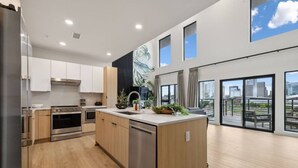 A modern kitchen with stainless steel appliances, wooden cabinets, and a large island with a sink. - Beverly Nash, Incredible Skyline Views! Pool & Gym, Walk to Broadway (Nashville)