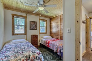 Une chambre avec deux lits, un ventilateur de plafond, des murs en bois et une fenêtre.