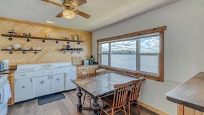Een keuken met een houten visgraat plafond, een eettafel met stoelen en uitzicht op het water door een groot raam.