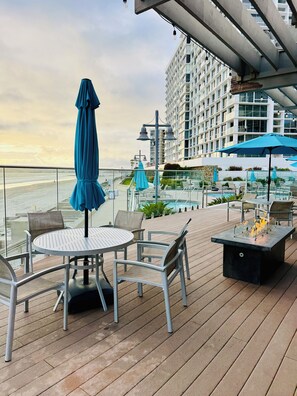 A deck with a round table and chairs, overlooking a pool and a beach. - Condo with stunning views of Pacific Ocean, Coronado Beaches & San Diego Bay! (Coronado)