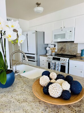 A modern kitchen with white cabinets, a stainless steel refrigerator, a microwave, and a sink. - Condo with stunning views of Pacific Ocean, Coronado Beaches & San Diego Bay! (Coronado)