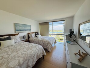 A hotel room with two beds, a large window with a view, and a small desk with a plant.