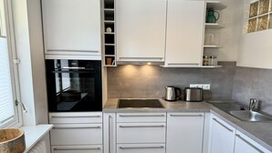 A modern kitchen with white cabinets, a built-in oven, a stainless steel sink, and a kettle.