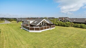 A modern house with a large deck, surrounded by a well-maintained lawn and a road in the background. - Cozy home in Harboøre (Harboøre)