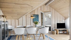 A modern, well-lit dining area with a wooden ceiling, a dining table with chairs, a vase with flowers, and a television on a wooden stand. - Cozy home in Harboøre (Harboøre)