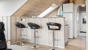 A modern kitchen with wooden paneling, a white refrigerator, and three black bar stools. - Cozy home in Harboøre (Harboøre)