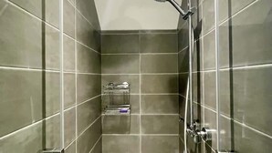 Eine moderne Dusche mit Handbrause und Wandarmatur, geflieste Wände und einem kleinen Ablagebereich für Toilettenartikel.