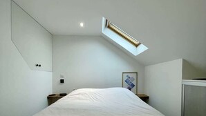 Ein Schlafzimmer mit einem großen Bett, einem Oberlicht, einem Spiegel und einem kleinen Nachttisch.
