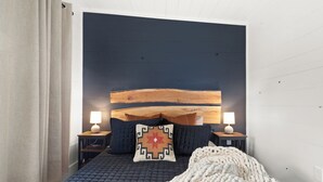 A bedroom with a dark blue headboard, two bedside lamps, a patterned pillow, and a knitted throw blanket. - Charming 2BR abode: Newly Restored, Full of Light, 2 Min to Stowe Center!"
(Stowe)