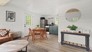 A modern kitchen with white cabinetry, a dining area with a wooden table and chairs, and a living room with a sofa and a coffee table. - Charming 2BR abode: Newly Restored, Full of Light, 2 Min to Stowe Center!"
(Stowe)