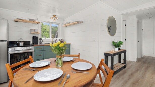 A modern kitchen with a dining area, featuring a wooden table set for four, a stove, and a sink. - Charming 2BR abode: Newly Restored, Full of Light, 2 Min to Stowe Center!"
(Stowe)