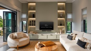 A modern living room with a large flat-screen TV, two sofas, a coffee table, and built-in shelves with decorative items. - Villa Divano by Sublime Samui Villas (Koh Samui)