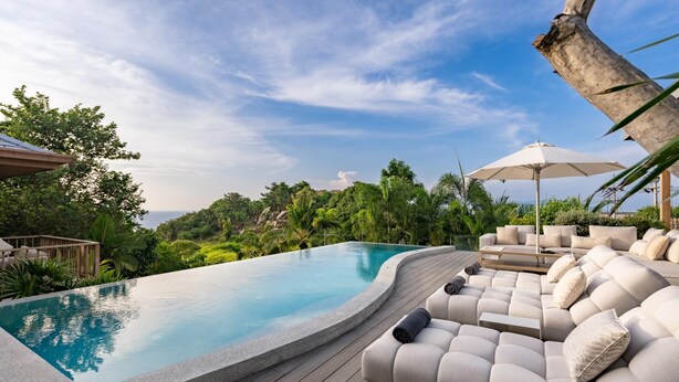 A pool with a curved edge, surrounded by a wooden deck and a beige sofa with cushions. - Villa Divano by Sublime Samui Villas (Koh Samui)